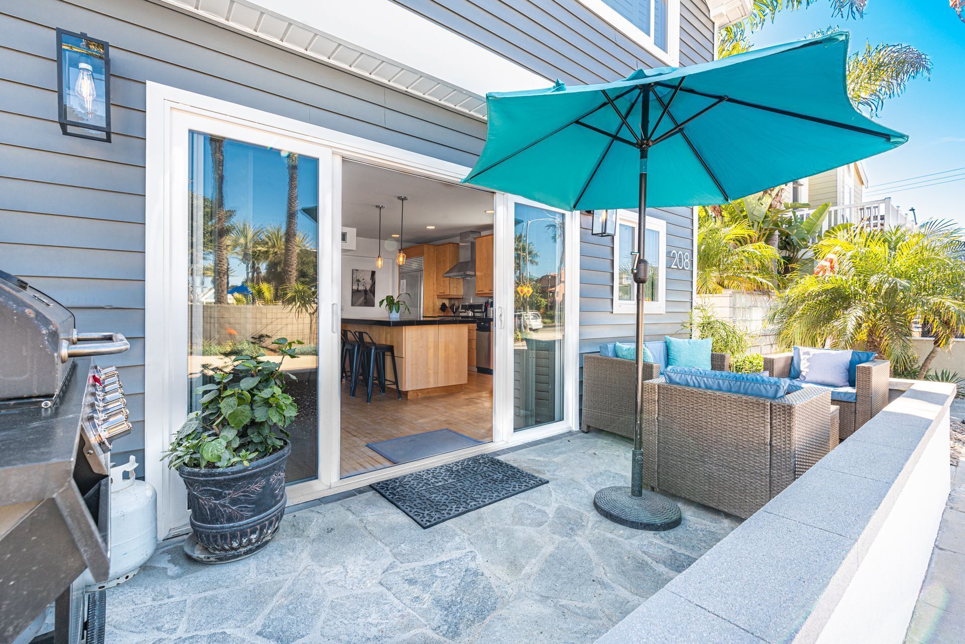 A patio with a blue umbrella, outdoor seating, a grill, and a potted plant.