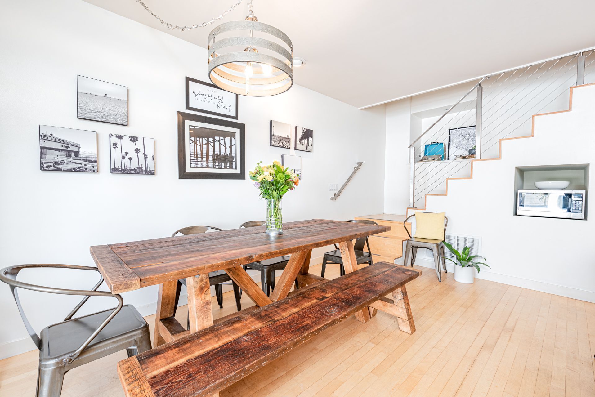 Un comedor con una mesa de madera y bancos, una escalera y cuadros en las paredes.