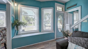 Una habitación con paredes color turquesa, suelo de madera, un asiento junto a la ventana, una puerta con panel de vidrio y una escalera.