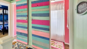 Una habitación con una puerta de color a rayas, una zona de ducha con un cartel y una cama con edredón azul y blanco.