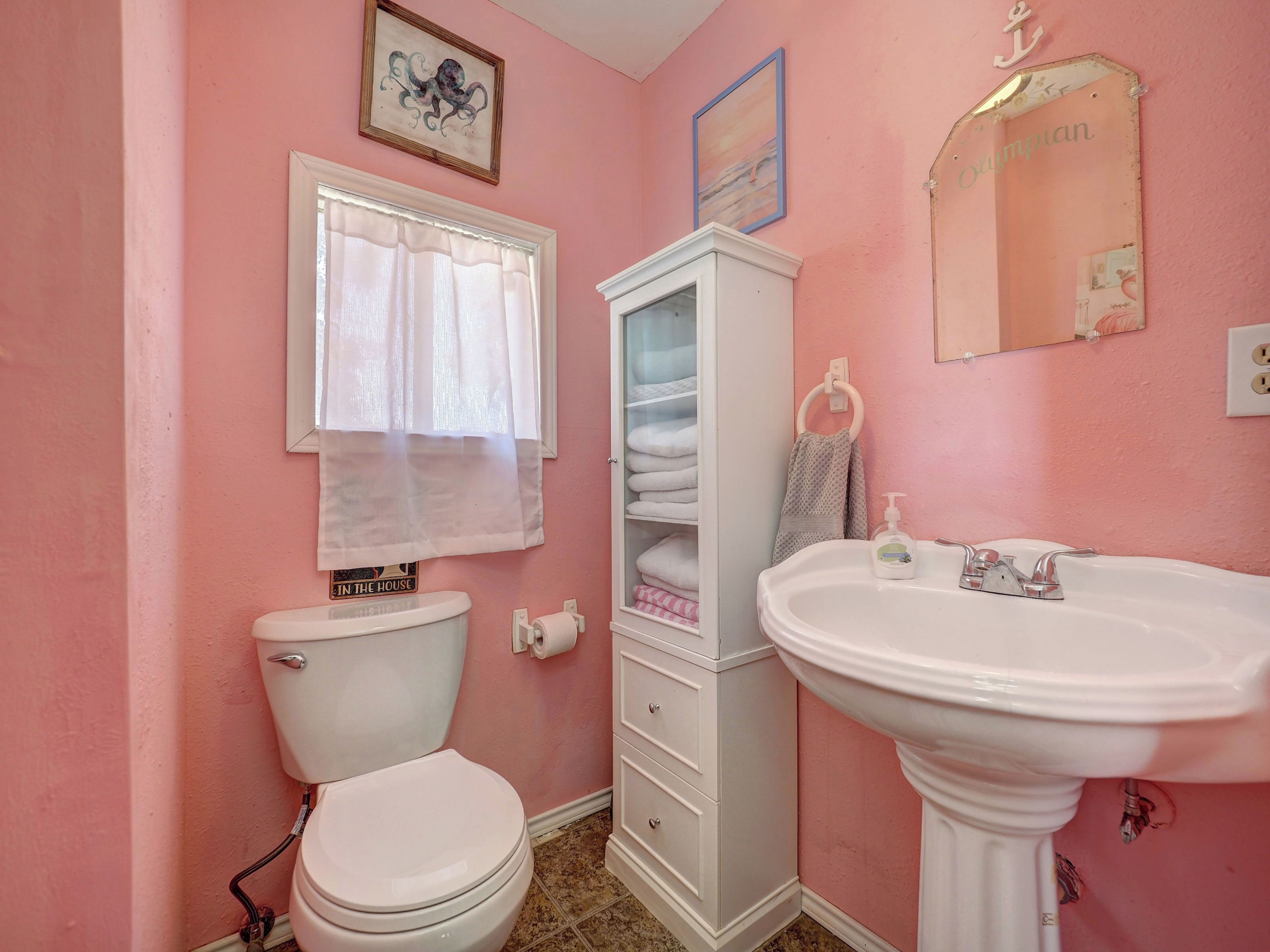 A bathroom with a toilet, a sink, a cabinet, and a window with a curtain.
