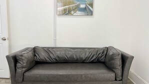 Un divano in pelle grigio in una stanza con una porta bianca e un quadro appeso al muro raffigurante una spiaggia.