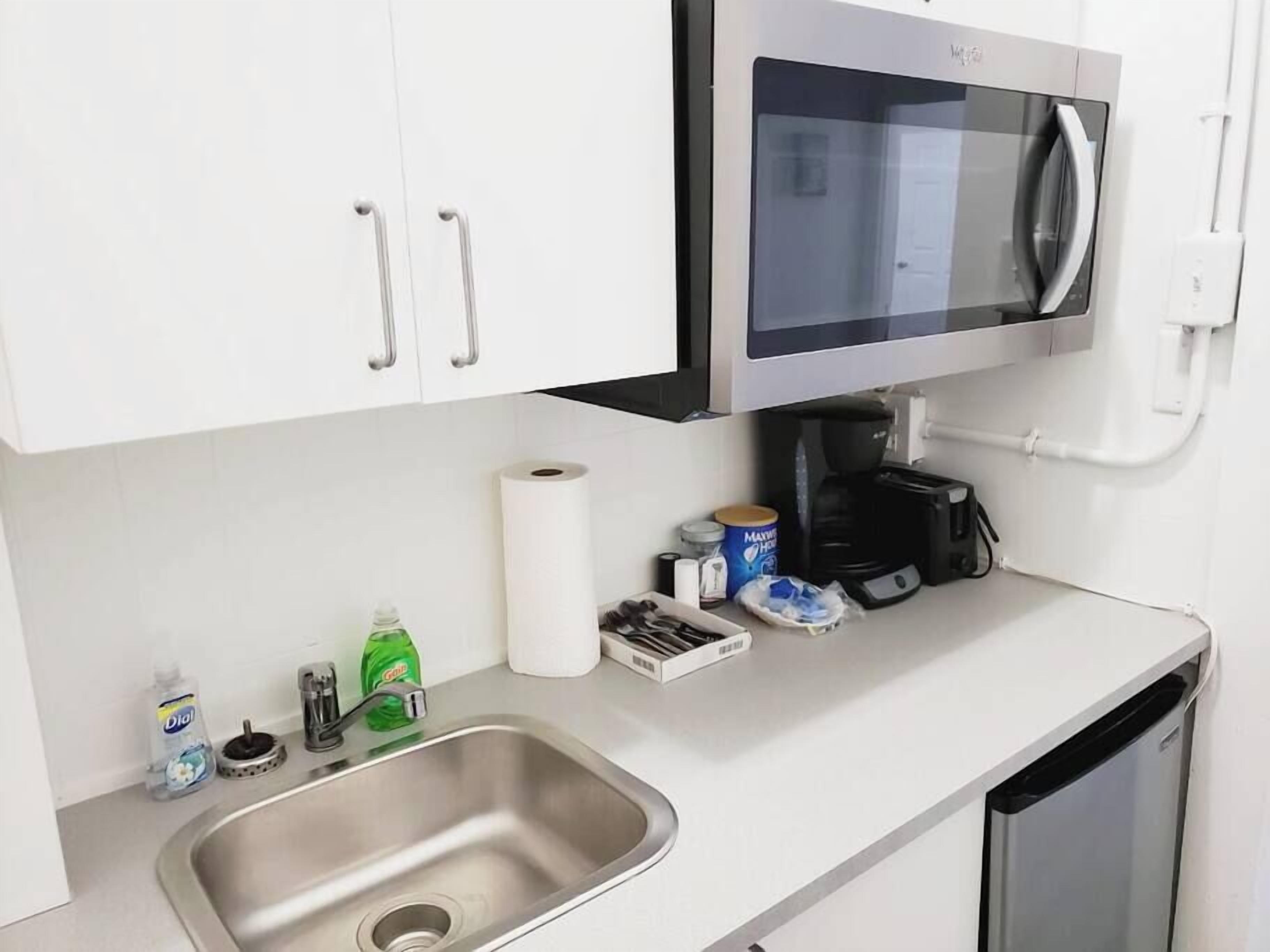 A kitchen with a stainless steel sink, a microwave, a coffee maker, and various kitchen items on the counter.