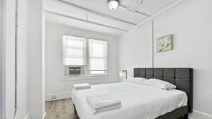 Una camera da letto moderna con un letto grande, lenzuola bianche, una testiera grigia e una finestra con persiane.
