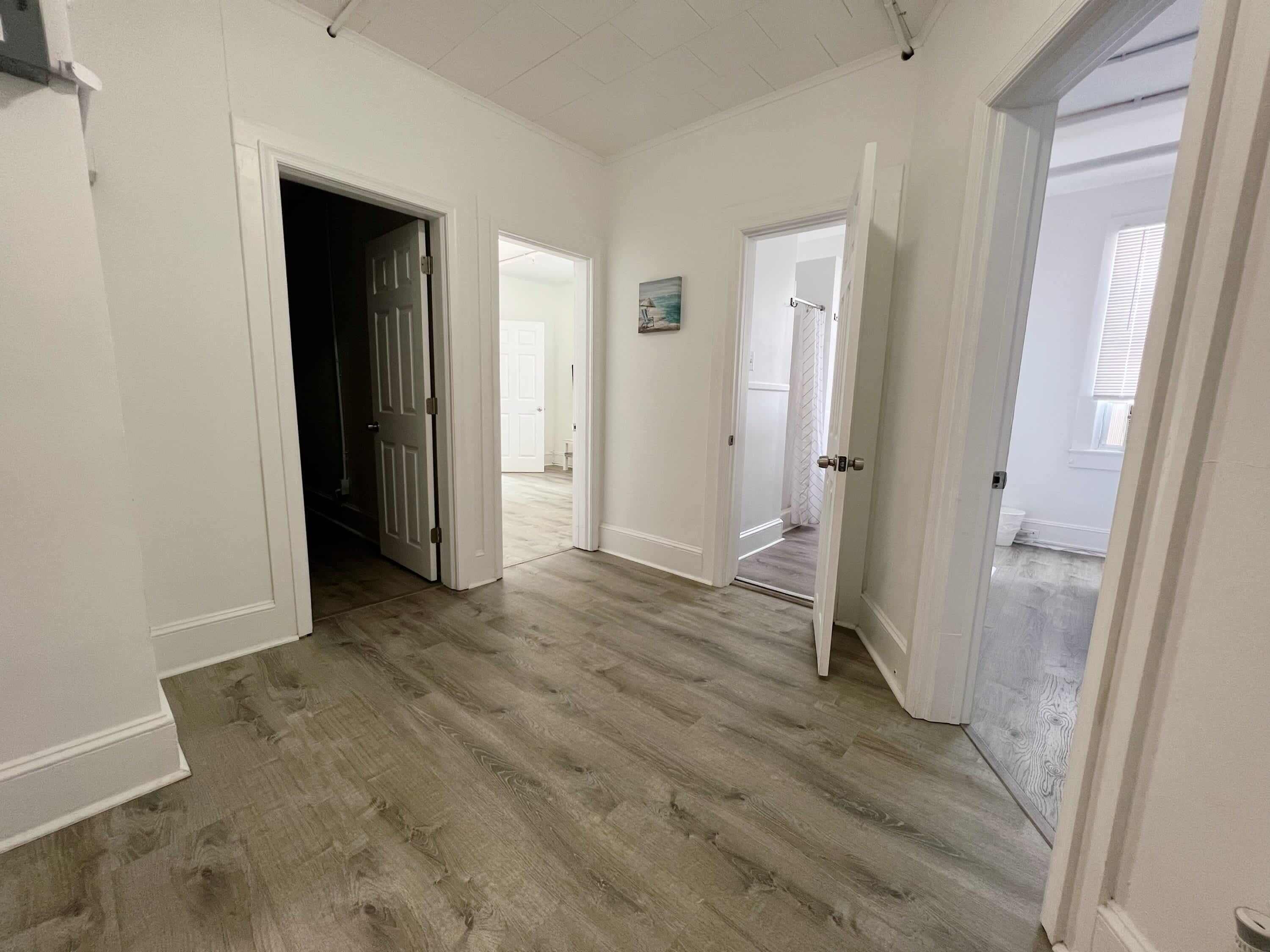 A spacious room with hardwood flooring, white walls, and multiple doorways leading to other rooms.