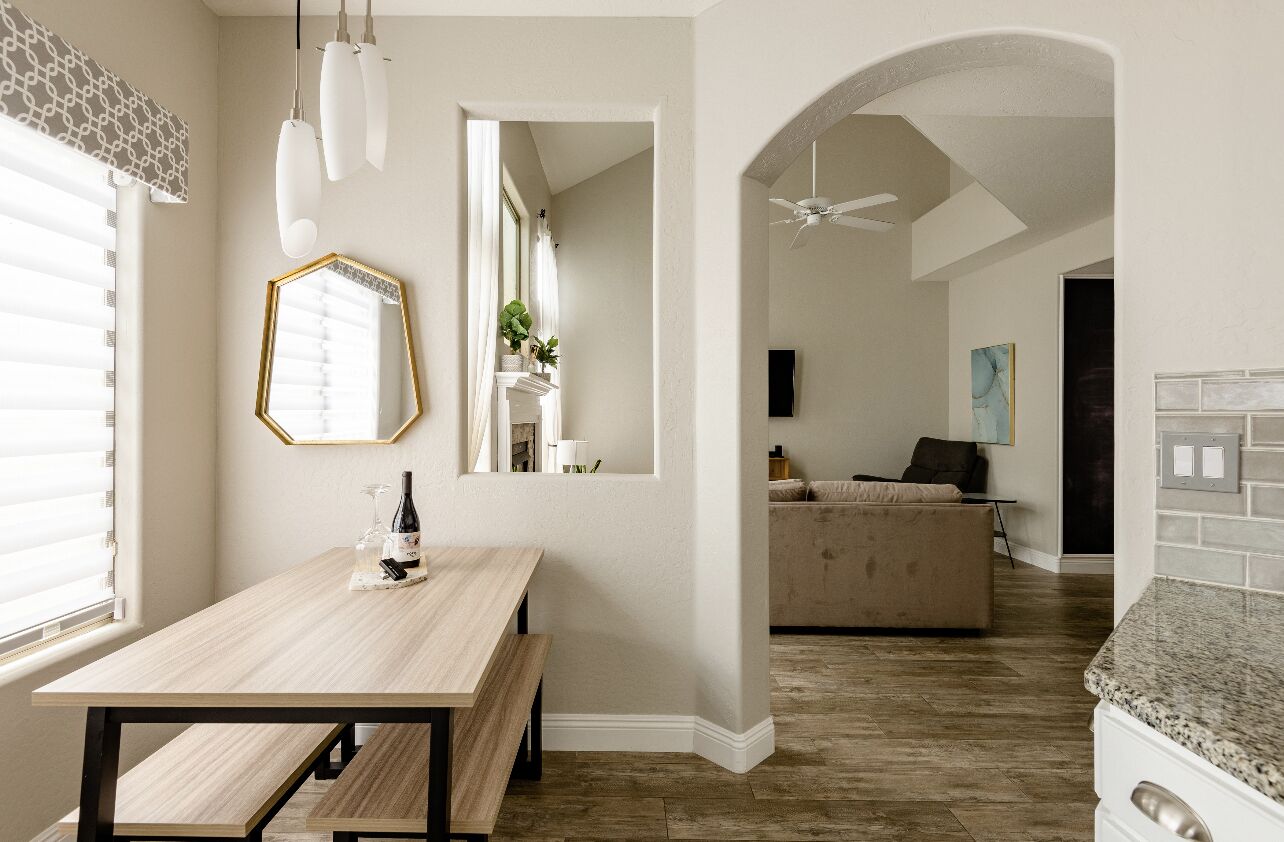 A modern kitchen with a wooden table, a ceiling fan, and a view into a living area with a sofa and a painting.