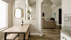 Een moderne keuken met een houten tafel, een plafondventilator en uitzicht op een woonruimte met een bank en een schilderij.