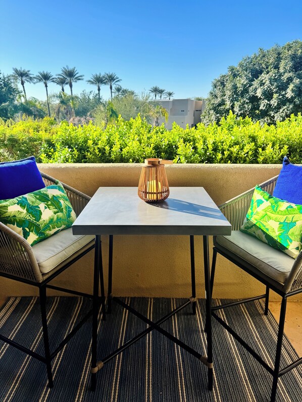 A table with two chairs, a candle, and a view of greenery and buildings in the background.