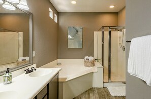 A modern bathroom with a large mirror, two sinks, a glass-enclosed shower, and a white towel hanging on the wall.