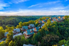 Un grupo de edificios tipo cabaña de troncos rodeados de un bosque denso, con cielo despejado arriba.