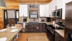 Una cucina moderna con mobili bianchi, zoccolo in mattoni, elettrodomestici in acciaio inossidabile e soffitto in legno.