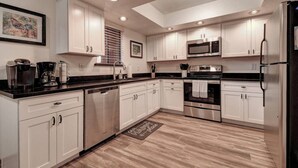 A modern kitchen with white cabinets, stainless steel appliances, and a black countertop. - So SnAZzy Ground Floor King (Phoenix)