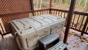 A covered outdoor seating area with a grill, a hose, and a wooden deck with fallen leaves. - Country Charm Cabin  (Hillsboro)