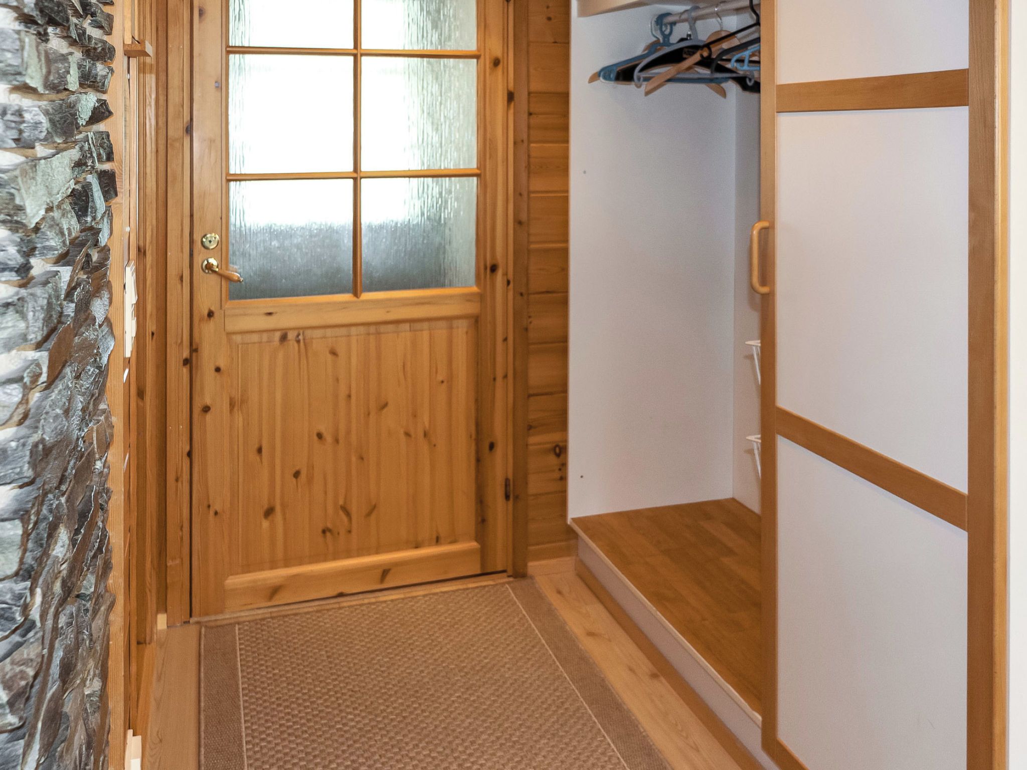 Una puerta de madera con un ventanal de vidrio esmerilado, una pared de piedra y un piso de madera con un tapete.