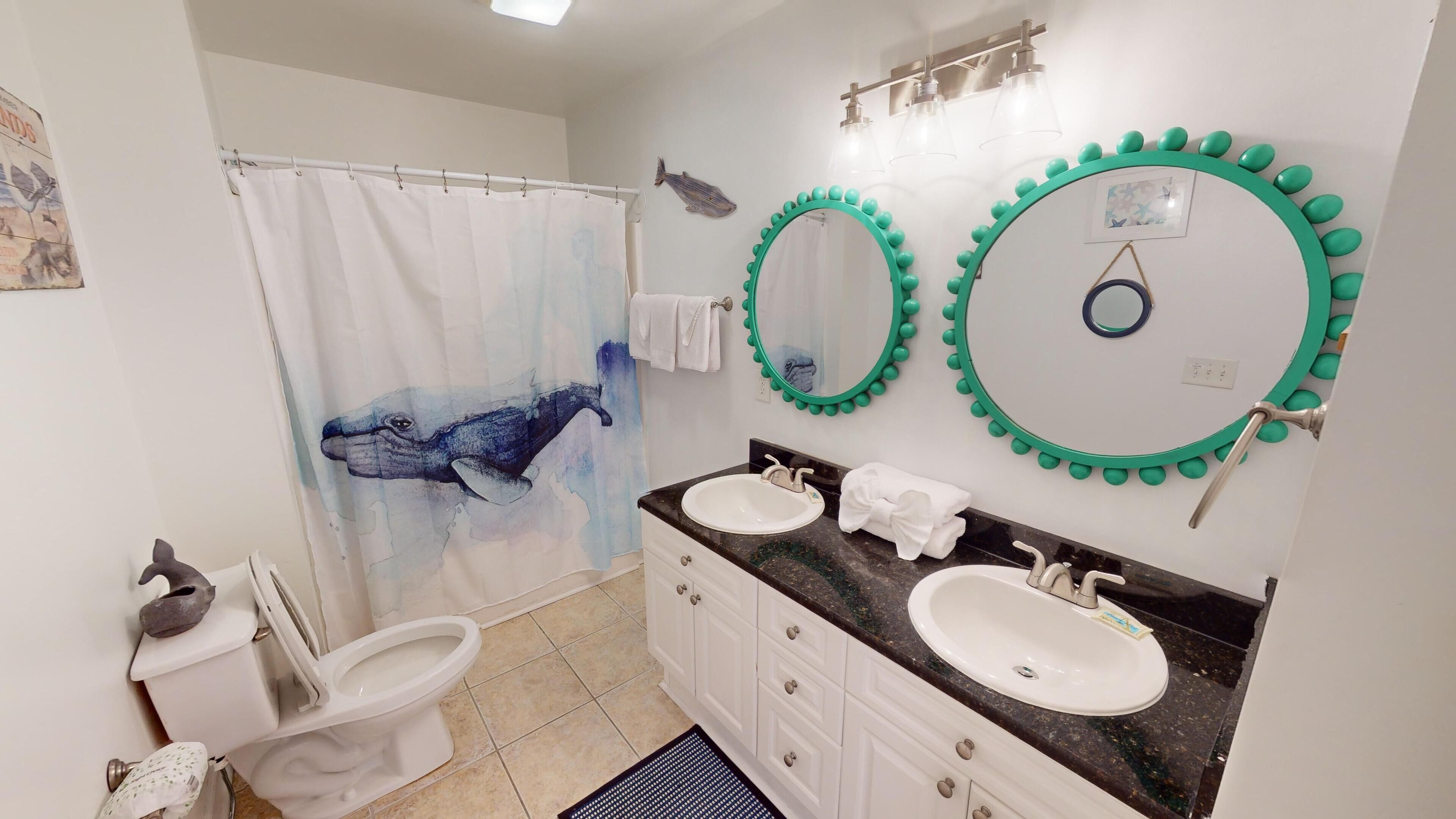 Un baño con dos lavamanos, una cortina de ducha con diseño de ballena y dos espejos montados en la pared con detalles verdes.