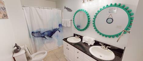 Un baño con dos lavamanos, una cortina de ducha con diseño de ballena y dos espejos montados en la pared con detalles verdes.