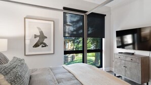A modern bedroom with a large window, a bed, a TV, and a cabinet. - Luxury Condo, Downtown Asheville (Asheville)