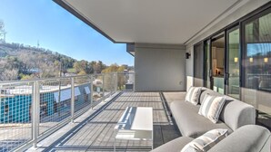 A balcony with a sofa and a table, a view of a hilly landscape, and a metal railing. - Luxury Condo, Downtown Asheville (Asheville)