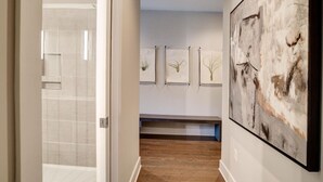 A hallway with a tiled shower area, a wooden floor, and three framed artworks on the wall. - Luxury Condo, Downtown Asheville (Asheville)
