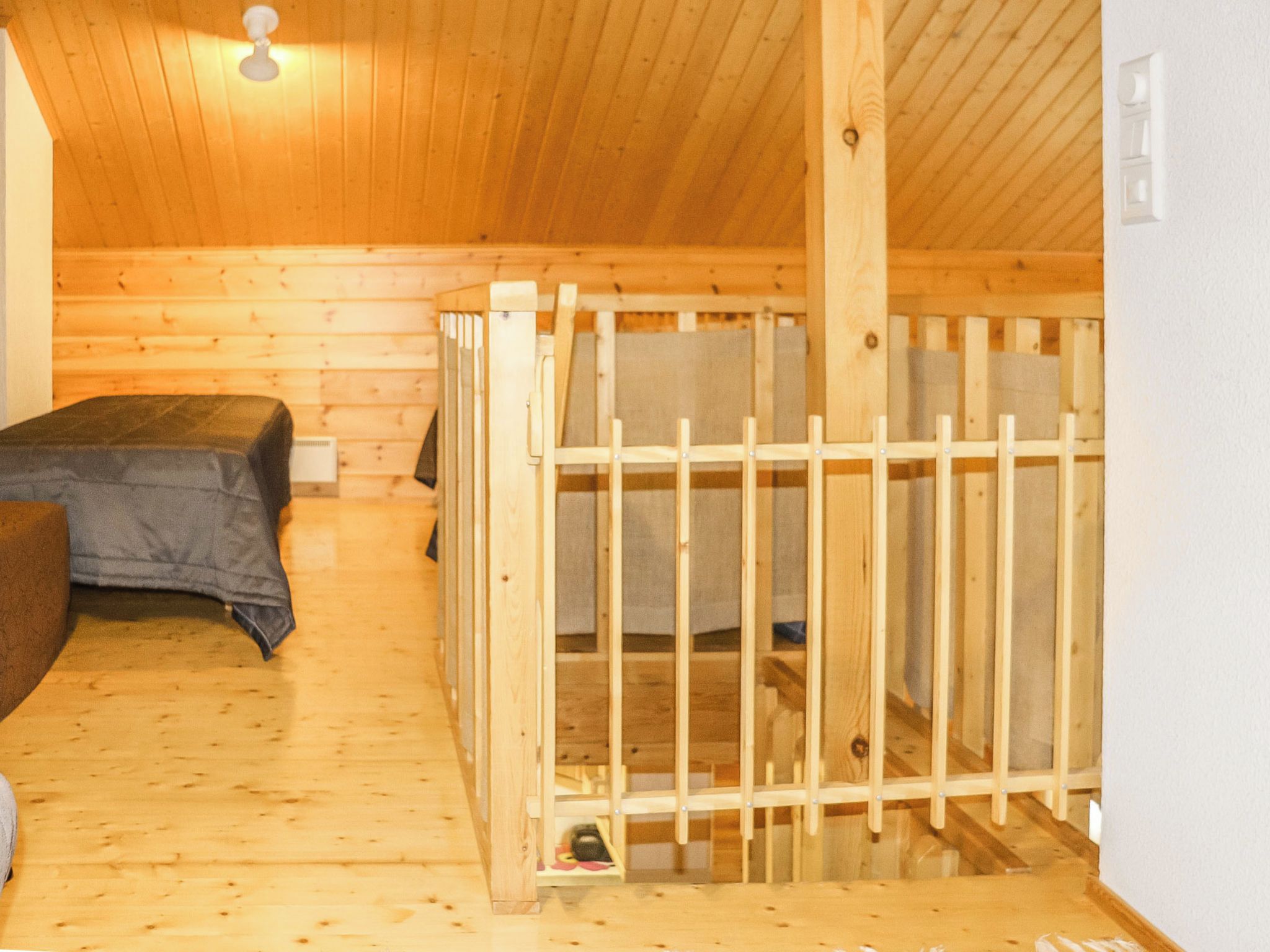 A wooden cabin with a bunk bed, a single bed, and a small wooden structure, possibly a playpen or storage.