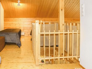 Una baita di legno con un letto a castello, un letto singolo e una piccola struttura in legno, forse un recinto giochi o un mobiletto.