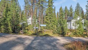 Maalaistie, jonka pinta on päällystetty soralla, ja jota ympäröivät tiheät havupuut sekä kaksi taloa, joiden piiput näkyvät selvästi.