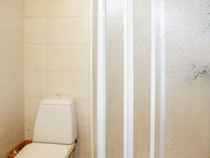 A modern bathroom with a toilet, shower, and trash bin.