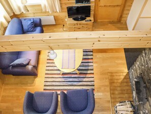 Una stanza con soffitto in legno, televisore, divano, poltrona e tappeto decorato.