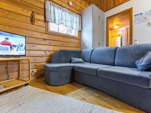 Ett modernt vardagsrum med en grå hörnsoffa, en platt-TV, träpanel på väggarna och en liten matta.
