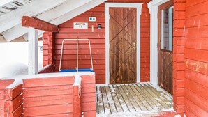 Punainen puinen rakennus, jossa on puinen ovi, kyltti, jossa lukee ”Lomapesa 2B”, ja puinen portaikko, joka johtaa katettuun kuistille.
