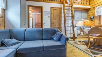 Een gezellig chalet binnen met een blauwe bank, houten wanden, een keukenhoek en een vide.