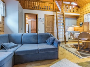 A cozy cabin interior with a blue sofa, wooden walls, a kitchen area, and a loft space. - Lomapesä 2b by Interhome (Puolanka)