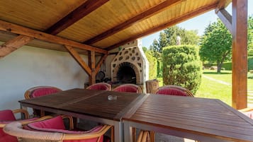 Een terras buiten, met een steenoven, rieten meubels en uitzicht op de tuin.