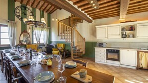 A spacious dining area with a long wooden table set for a meal, a staircase leading to an upper level, and a kitchen with white cabinets. - Stunning private villa for 10 guests with hot tub, WIFI, A/C, private pool, TV and terrace (Lucignano)