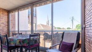 A balcony with a dining table and chairs, a cushioned chair, and a view of buildings and power lines. - Plein Soleil by Interhome (Arcachon)