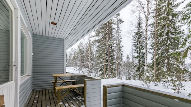 Eine Holzterrasse mit Tisch und Bänken, umgeben von schneebedeckten Bäumen.