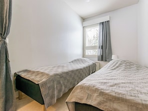 Una habitación pequeña y sencilla con dos camas individuales, una ventana con cortinas y un radiador.