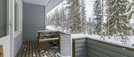 Eine Holzterrasse mit Tisch und Bänken, umgeben von schneebedeckten Bäumen.
