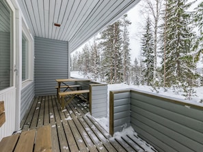 Une terrasse en bois avec une table et des bancs, entourée d’arbres couverts de neige.
