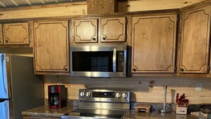 Eine Küche mit Holzausstattung, einer Edelstahl-Mikrowelle, einem Backofen und einem Kühlschrank.