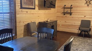 Ein rustikales Holzinterieur mit einem Esstisch, Stühlen, einem Kamin und einem Deckenventilator.