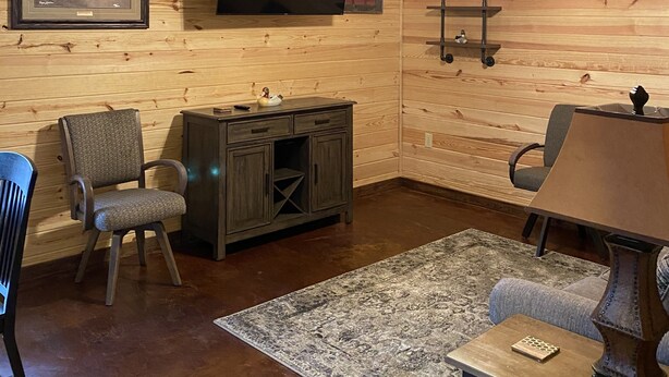 Ein rustikales Interieur mit Holzwänden, einem Wand-Fernseher, einem Deckenventilator und einem aufgehängten Hirschschädel.