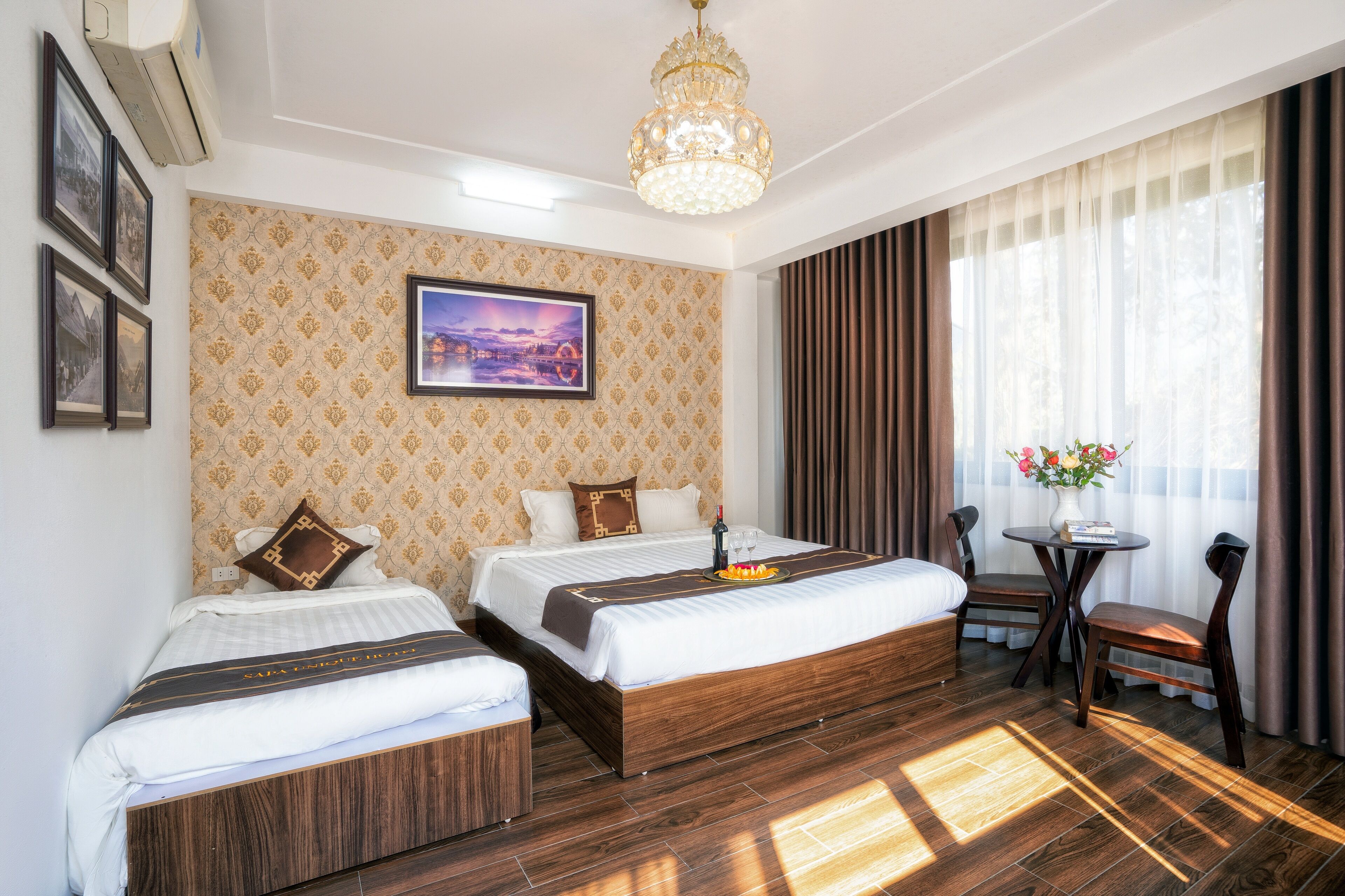 Une chambre d’hôtel avec deux lits, un lustre, une table à manger avec des chaises et une fenêtre avec des rideaux.
