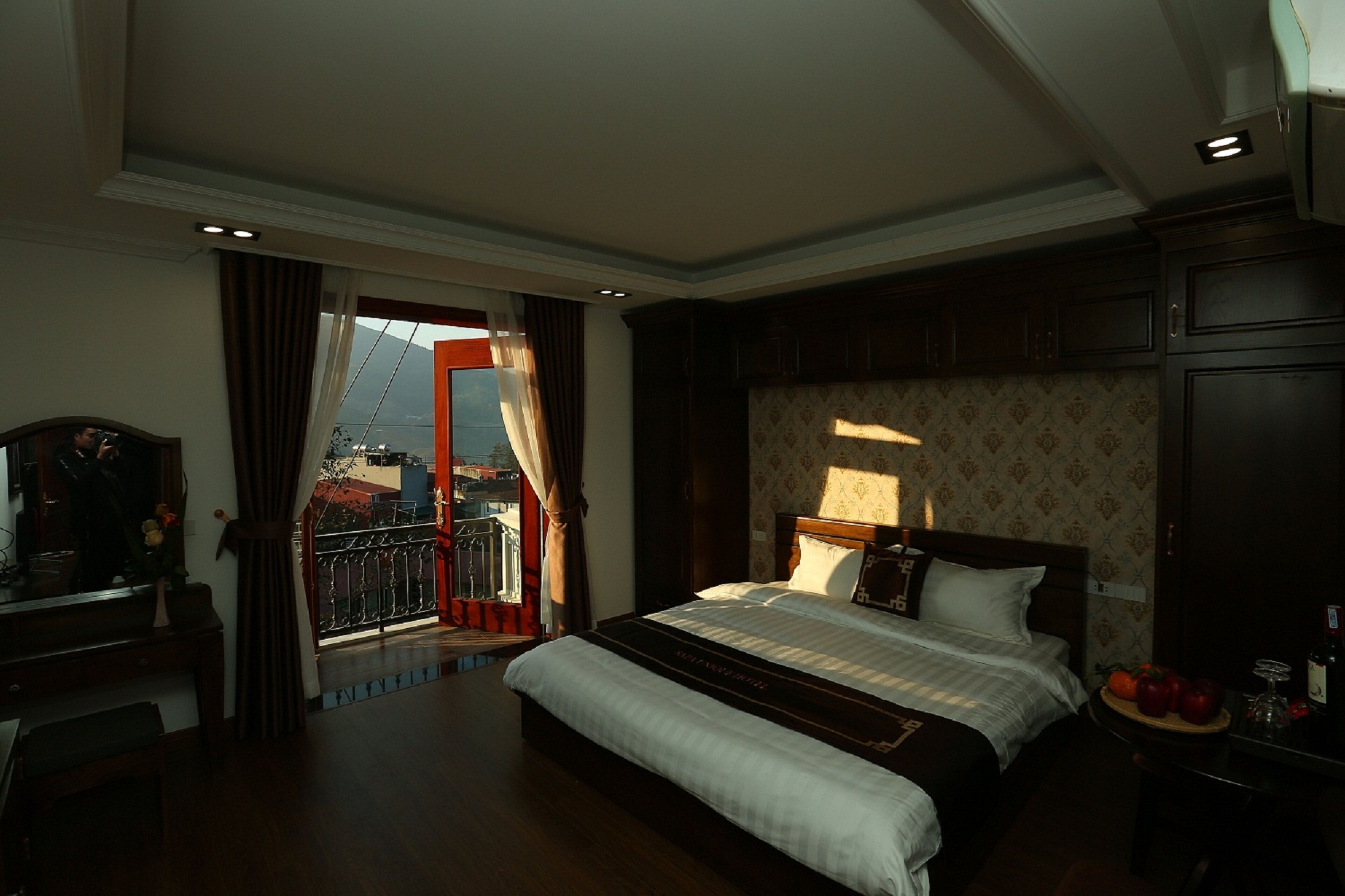 A hotel room with a large bed, a desk, and a view of a cityscape through a window.