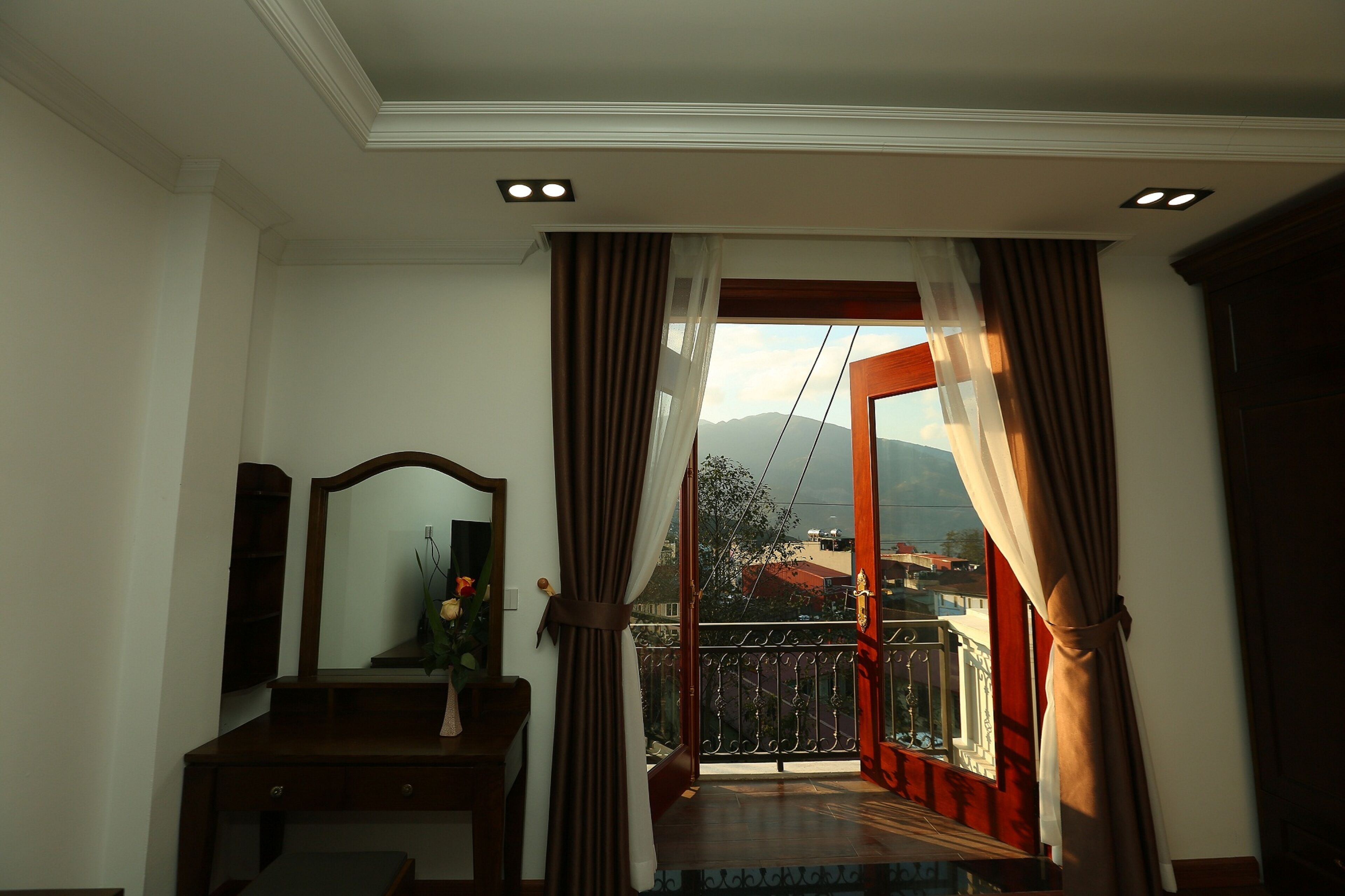A room with a wooden desk, a mirror, and a view of a balcony with a railing.