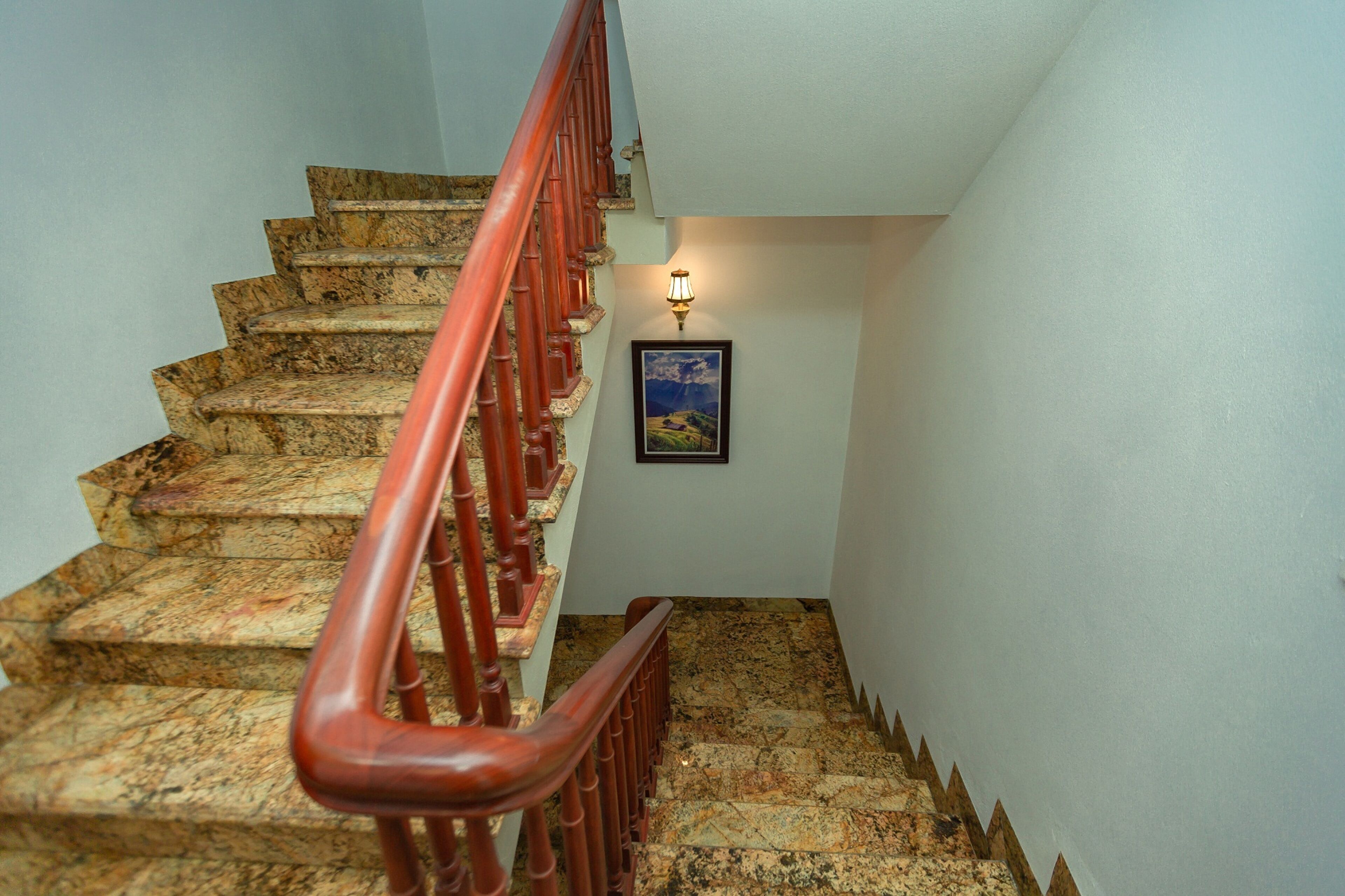 A staircase with a red handrail, granite steps, and a framed picture on the wall.