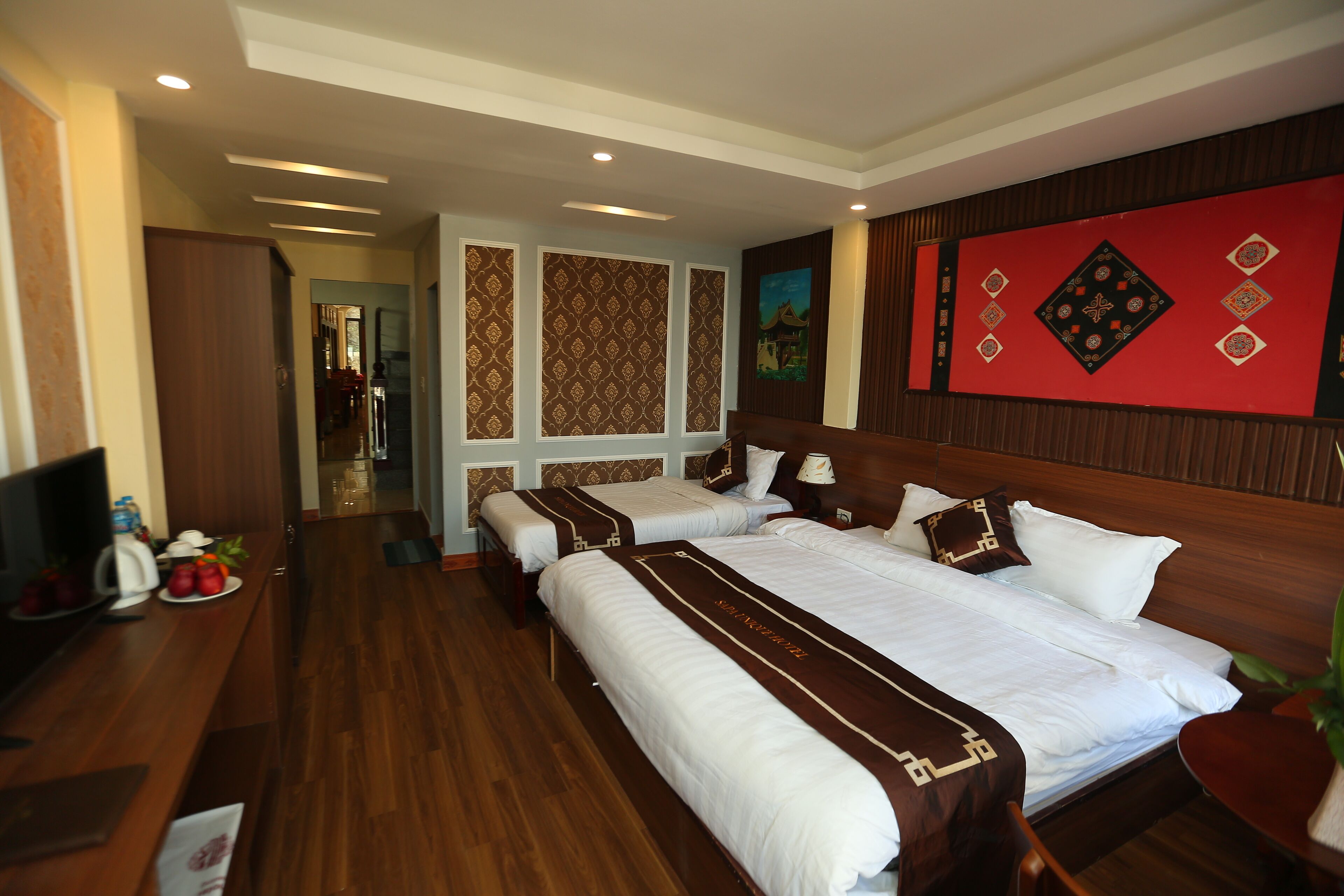 A hotel room with two beds, a wooden floor, a TV, and a dining area with a table and chairs.