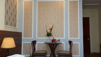Une chambre d’hôtel avec un lit, deux chaises, une petite table sur laquelle est posé un vase de fleurs et une lampe.