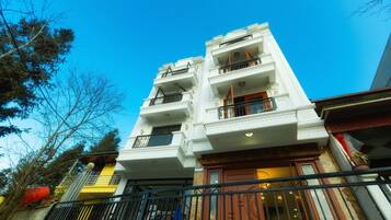 A multi-story building with balconies, a wooden door, and a metal railing.