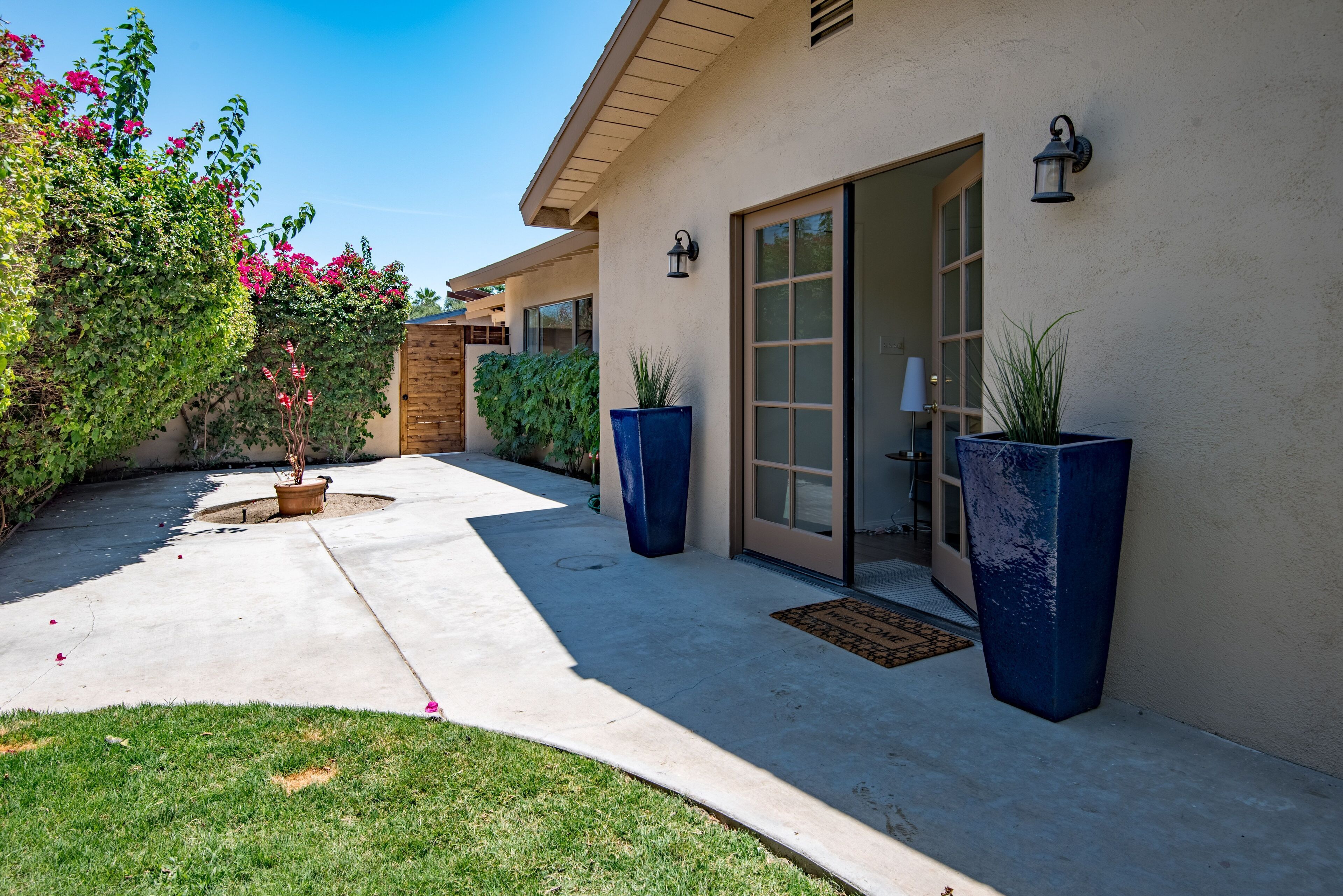 A building with a concrete patio, large potted plants, and a door leading to a covered entrance.